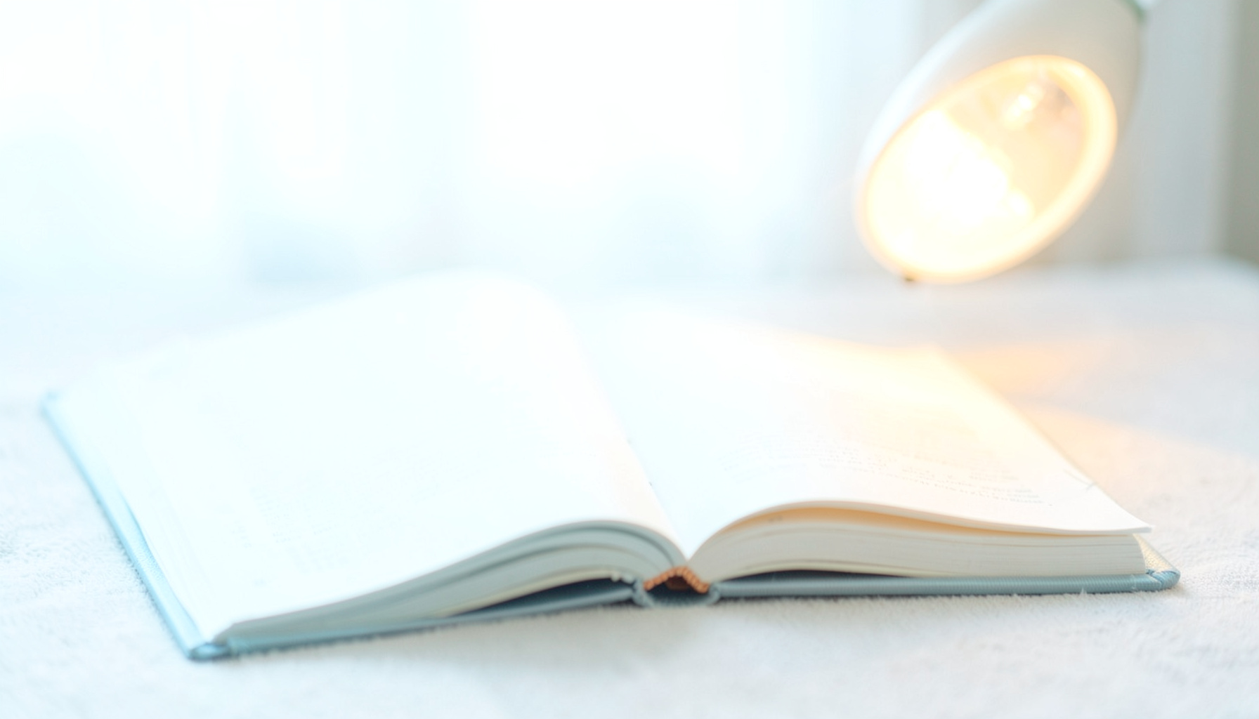 A bright, airy high-key photograph of an open book and warm reading light on a soft neutral surface