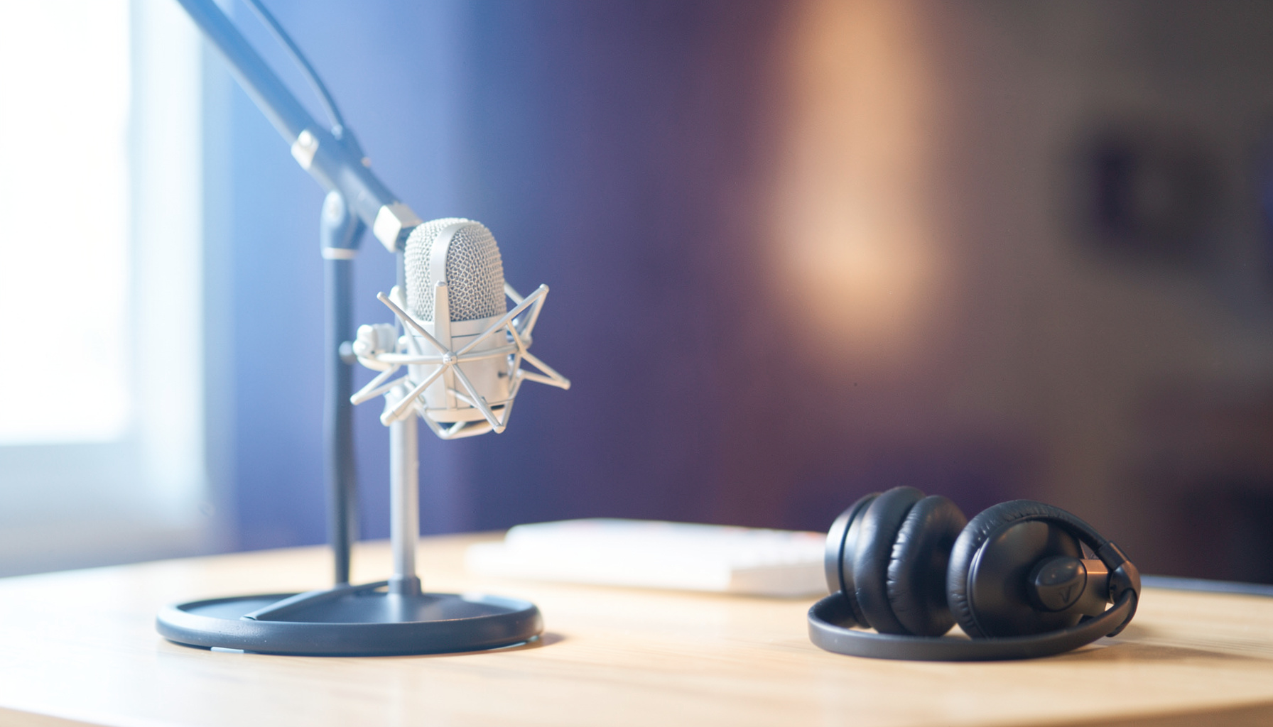 A warm, softly lit studio scene with a professional microphone on a desk, headphones nearby, and deep indigo and amber tones