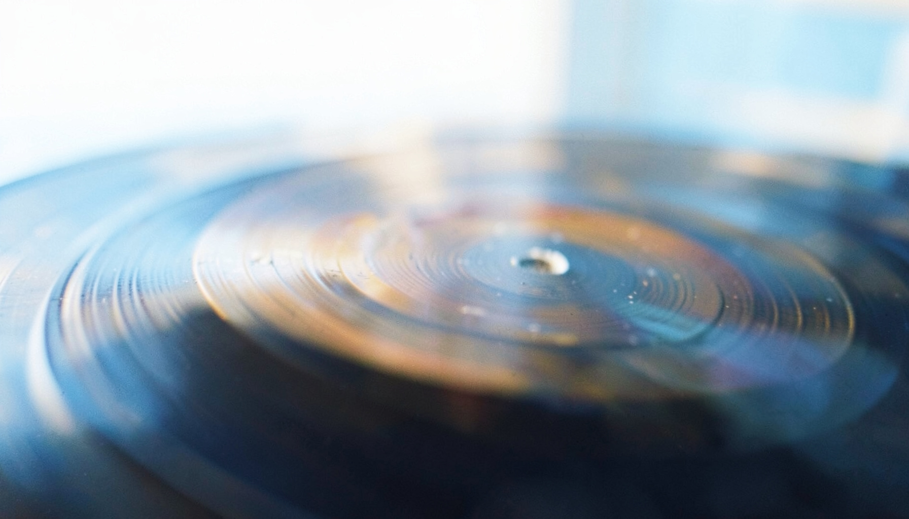 Warm amber and deep indigo tones wash over a close-up of vinyl record grooves, with soft bokeh light catching the ridges
