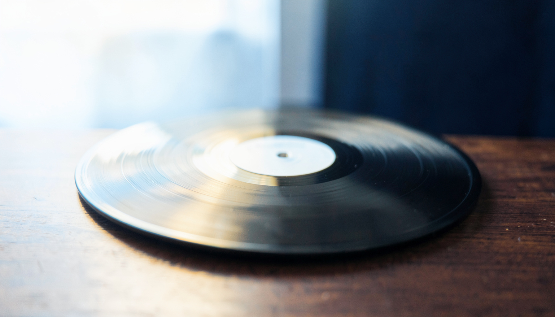 A softly lit vinyl record resting on a dark wooden surface with warm amber glow and deep navy tones